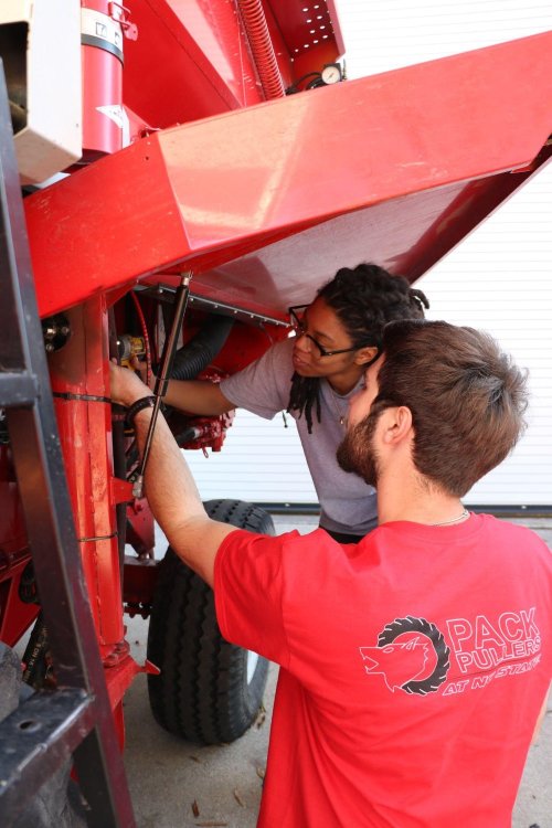 Alex Brown and a teammate working on a red piece of farm equipment