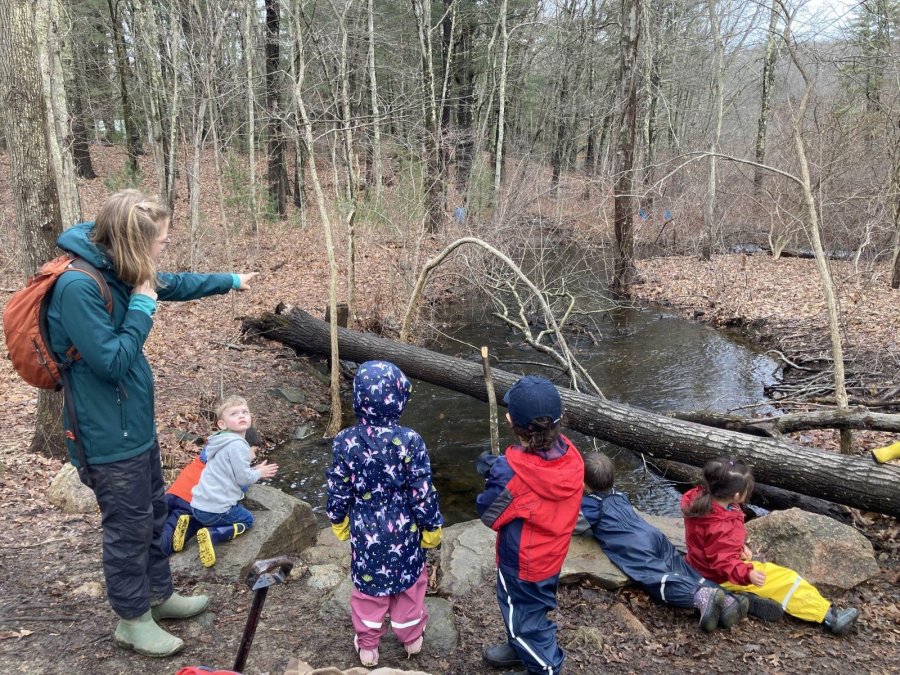 Eliza Foli pointing out something in the woods to a group of young children beside a stream